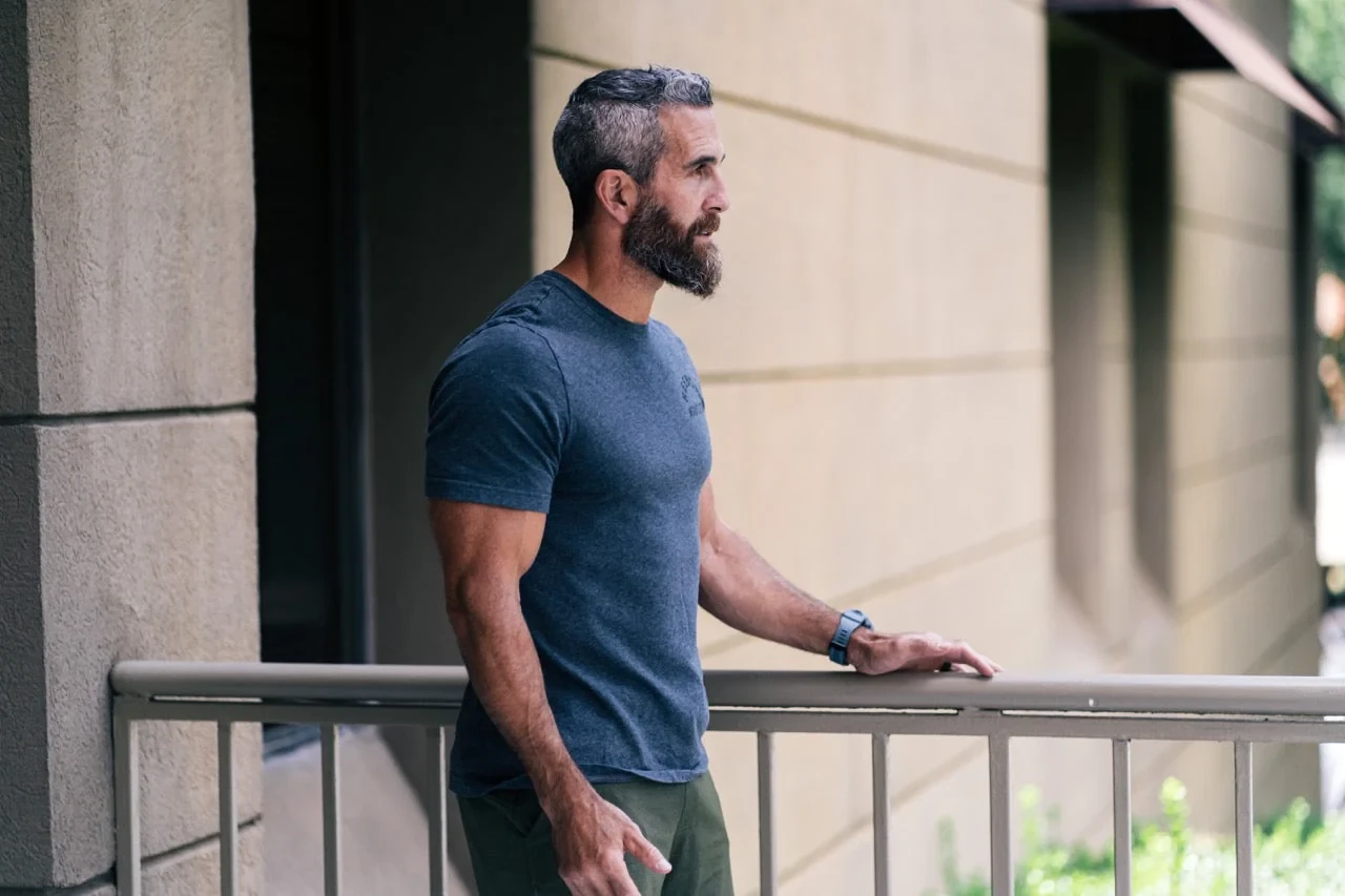 A man in a navy T-shirt leaning on a railing outdoors