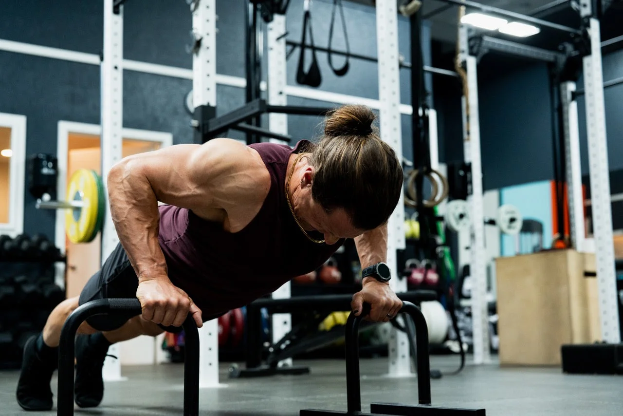 An athlete doing push-ups on parallettes in a gym