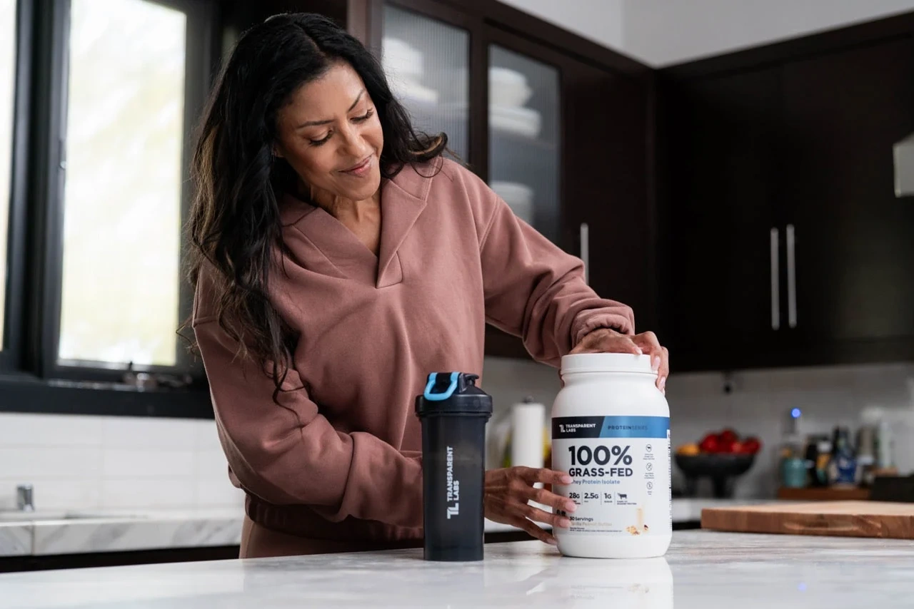 A woman with a whey tub and a shaker bottle in her kitchen